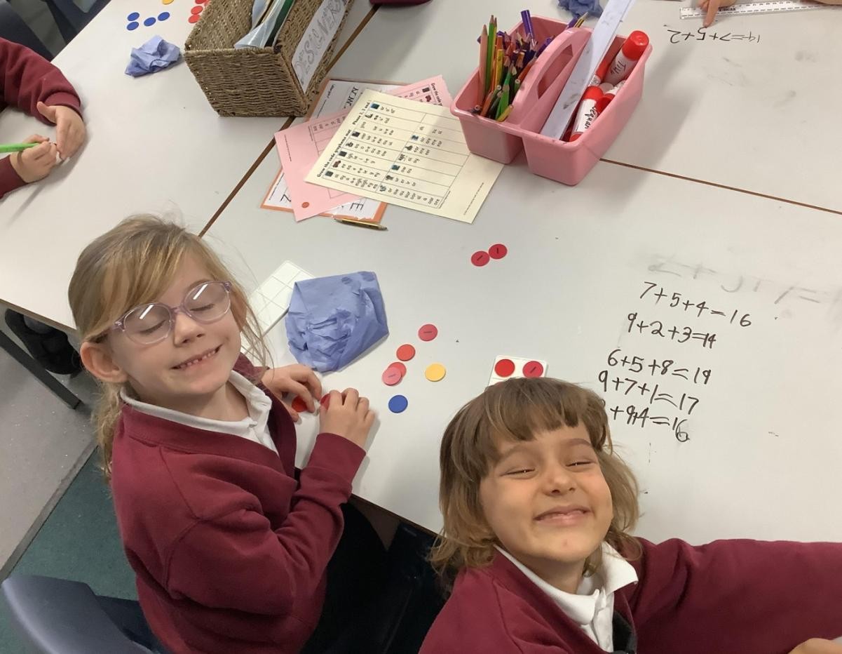 KS1 pupils using concrete resources to add three 1-digit numbers.