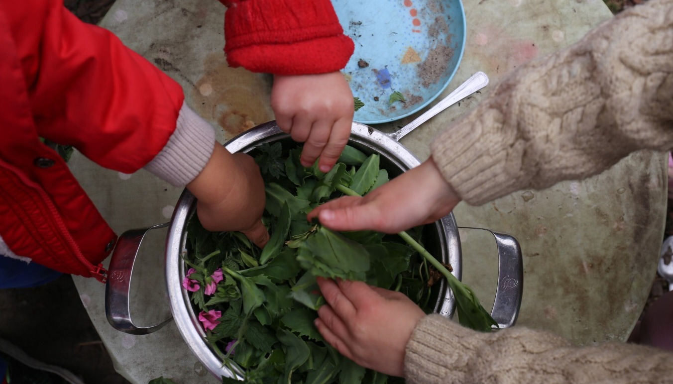 Children with hands in a bowl of leaves 