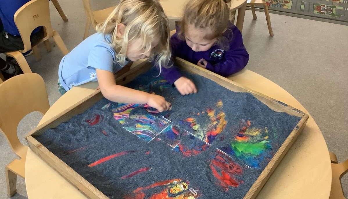 Children exploring tray of grey sand 