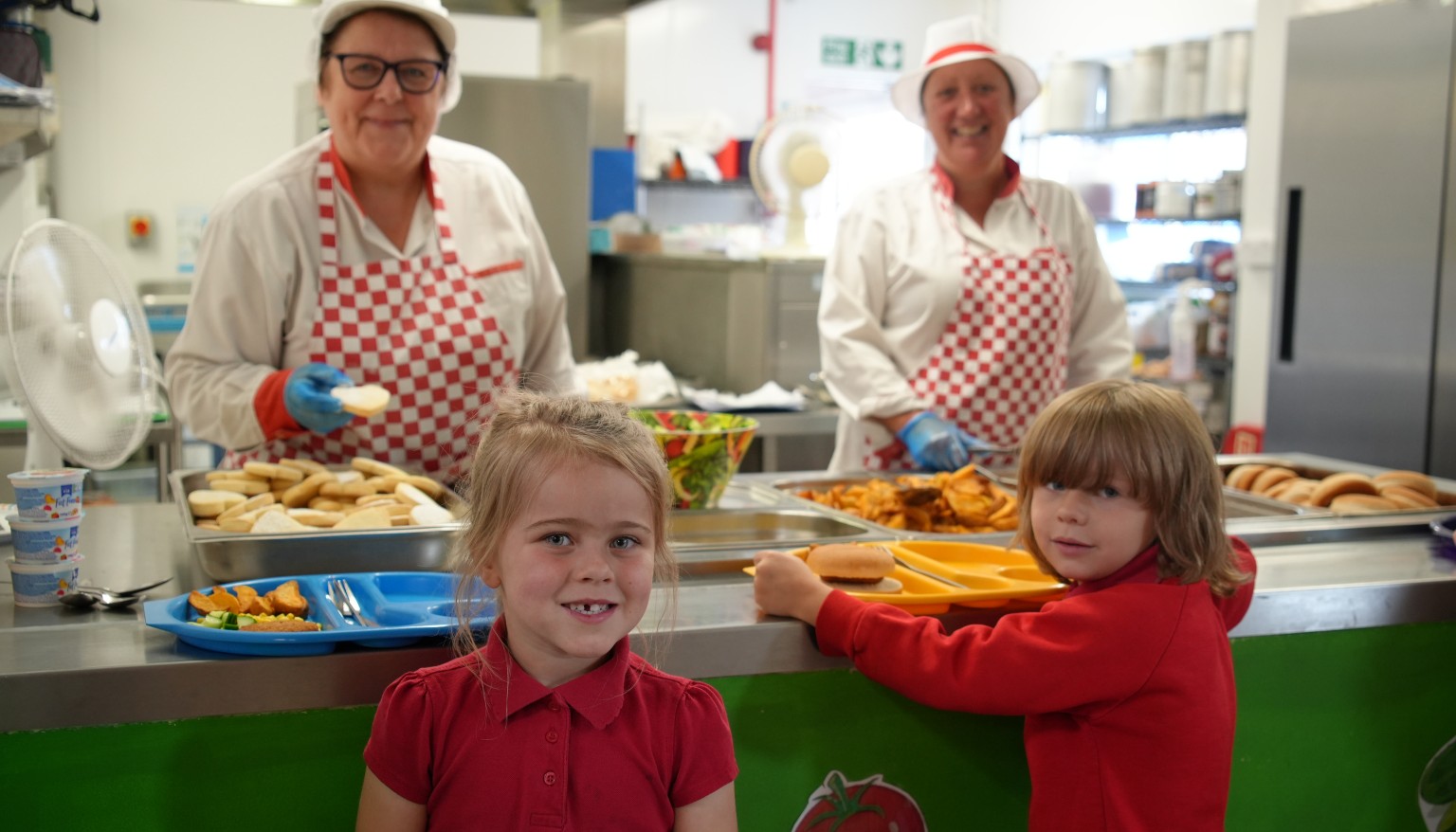Two children lining up to get their lunch from two cooks