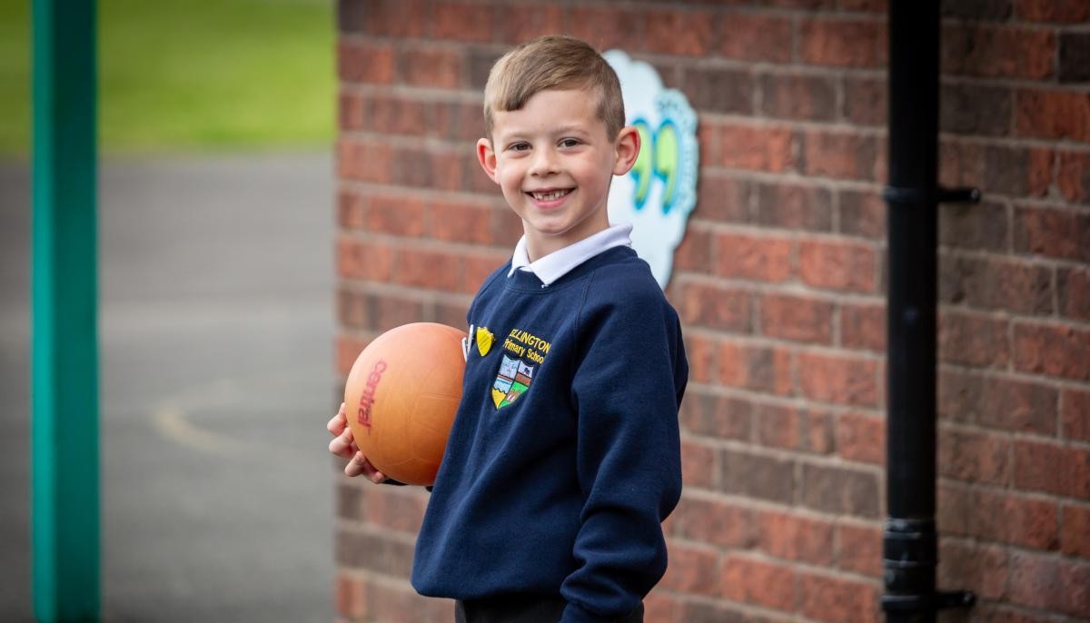 Child smiling at camera holding a orange ball