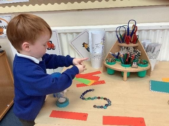 Pupil at craft table with paper strips and beads in the shape of an 'S'