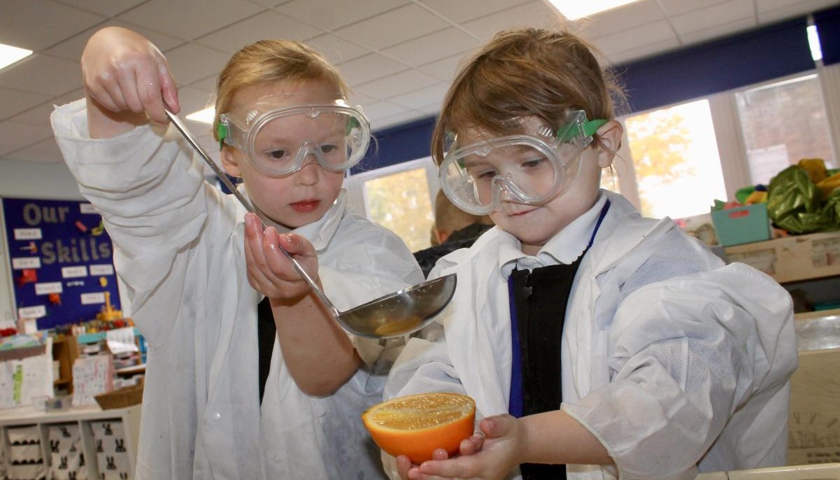 Pupils doing science experiements in lab coats and goggles