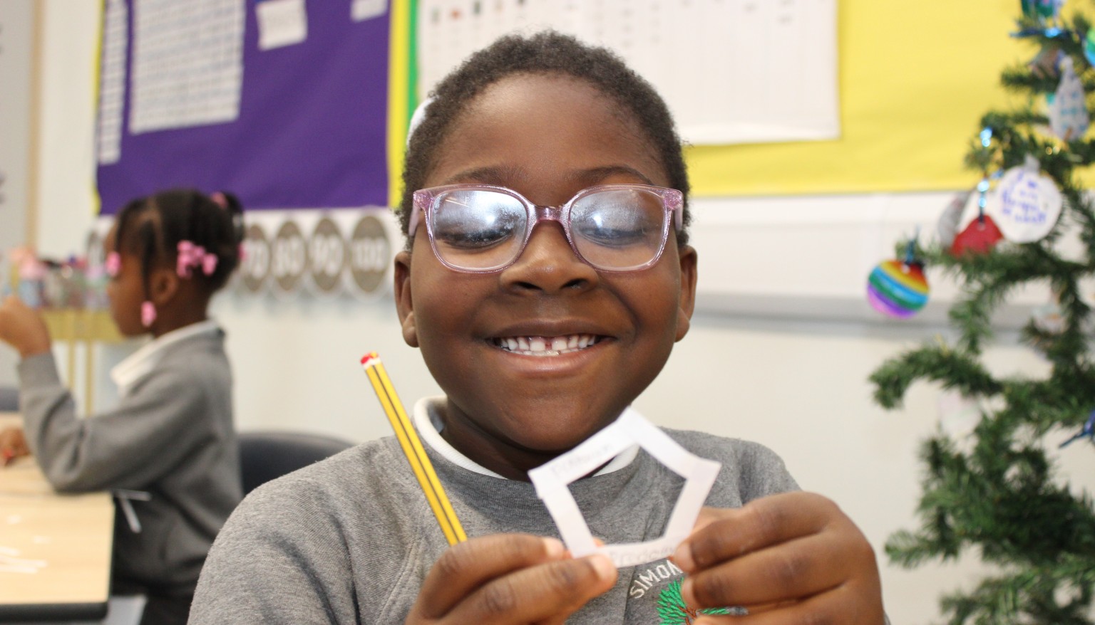 Child smiling at the camera holding up a pentagon shape