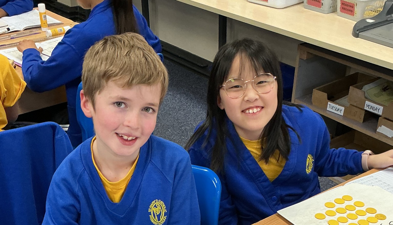 Two children smiling sat at a desk 