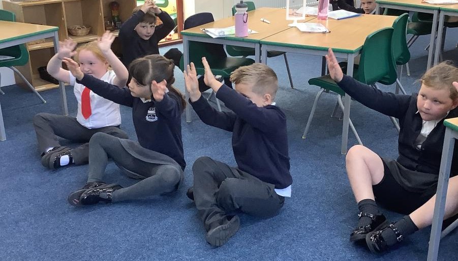 Children sat on the carpet with their arms in the air