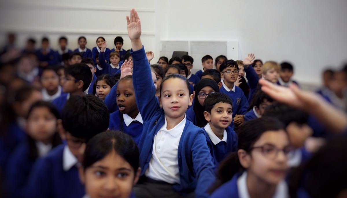 Assembly of children and a child holding up hand