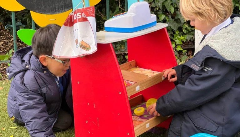 Two children playing in a role play shop outdoors