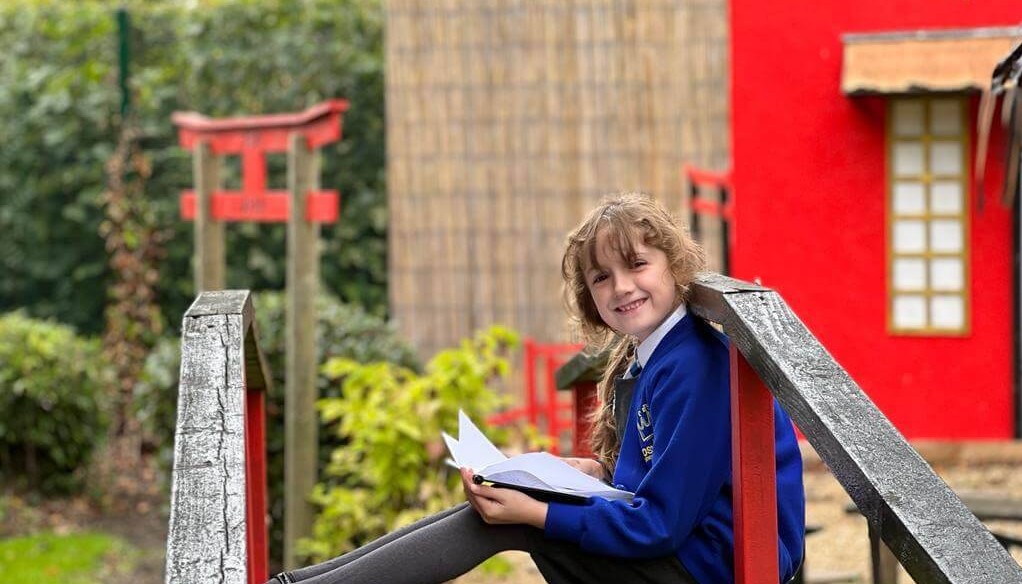 Child smiling at camera holding an open book on their lap 