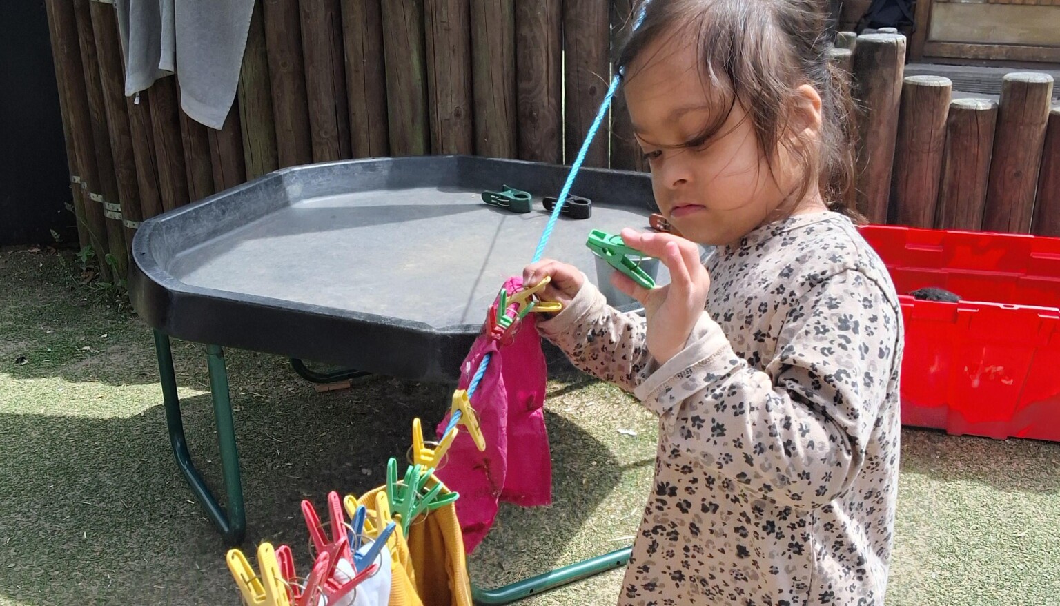 A young child using colourful plastic pegs to clip washing to a washing line.