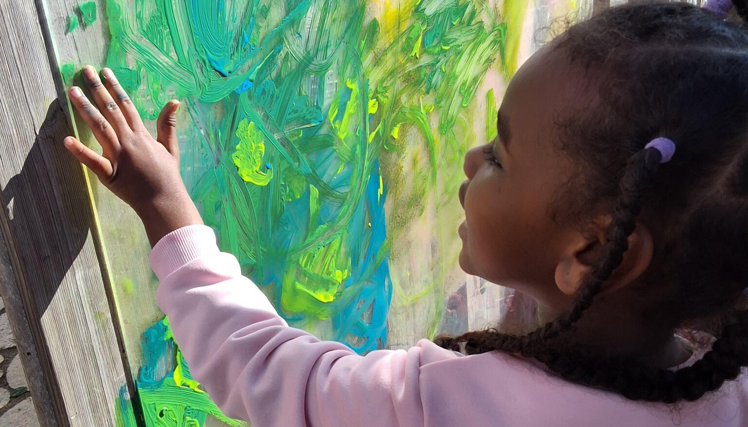 A young girl using her fingers to apply green paint to a perspects board.
