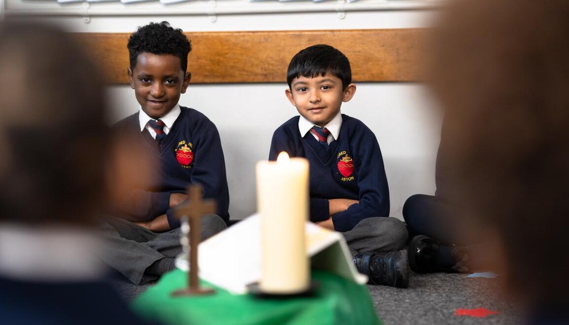 Cross and candle in foreground with two uniformed pupils behind