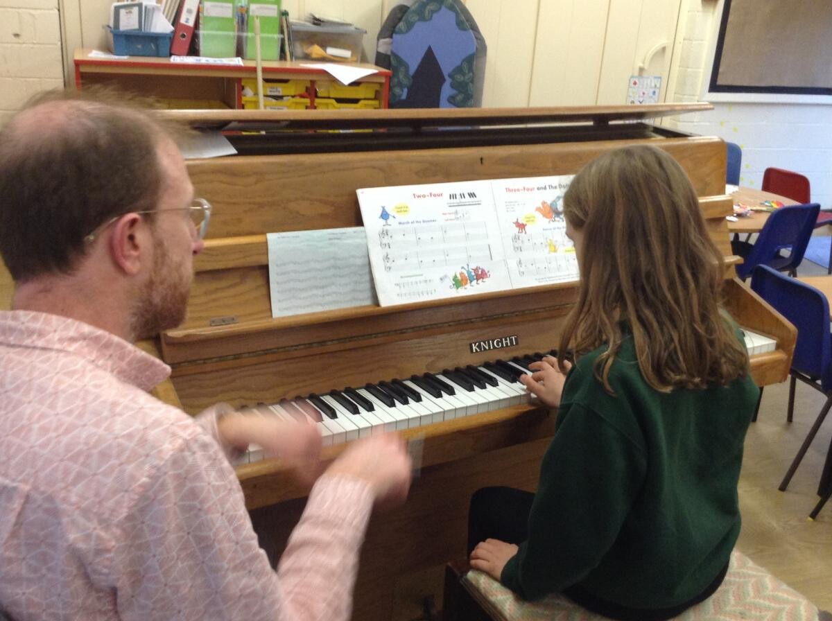 Pupil playing piano with teacher observing