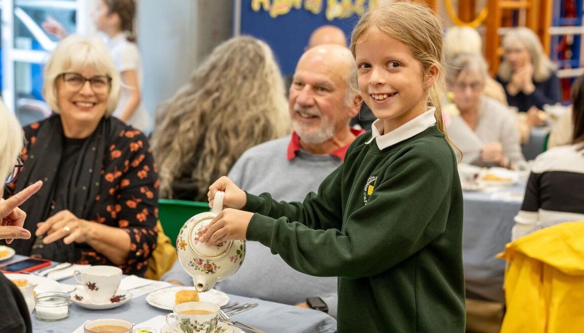 Smiling pupil pouring tea for guests at multi-generational tea party