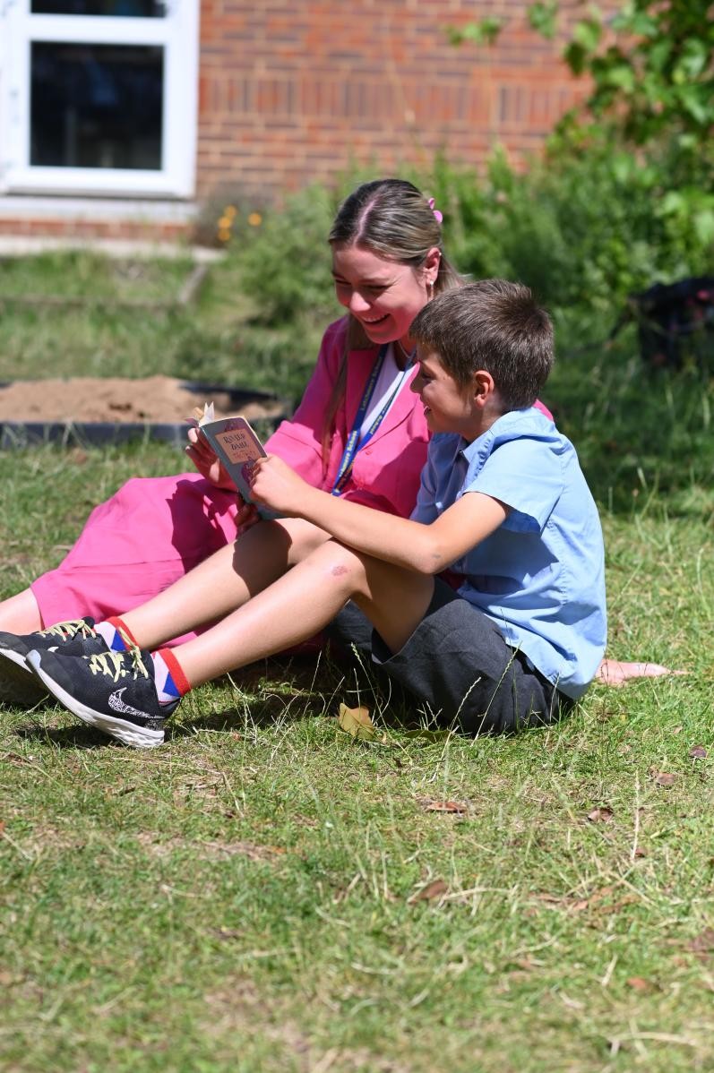 Adult and pupil reading outside on the grass